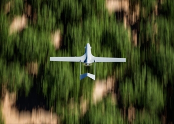 Top shot of a military UAV or drone (Bayraktar TB2) armed with missiles and flying over forest area with the ground blurred