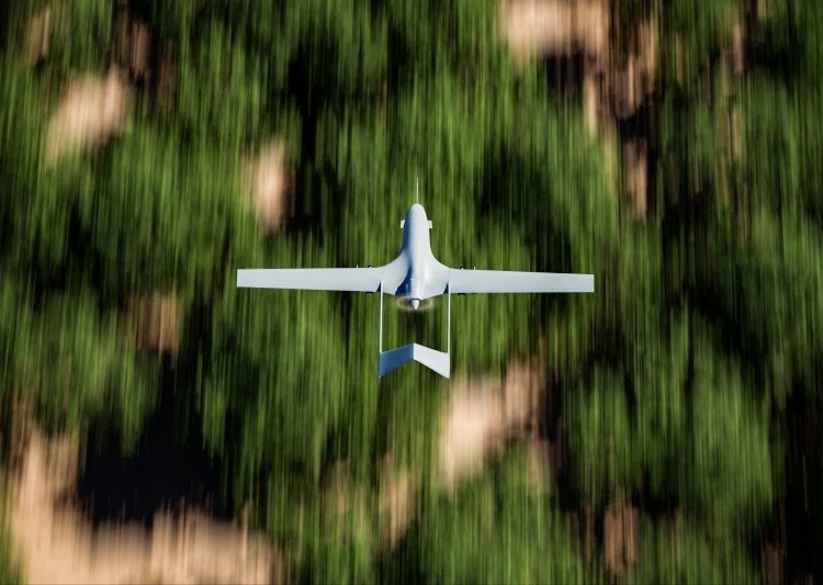 Top shot of a military UAV or drone (Bayraktar TB2) armed with missiles and flying over forest area with the ground blurred