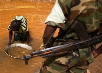 A soldier looks on as a woman pans for gold near an open pit at a mine in Central African Republic [File: Siegfried Modola/Reuters]